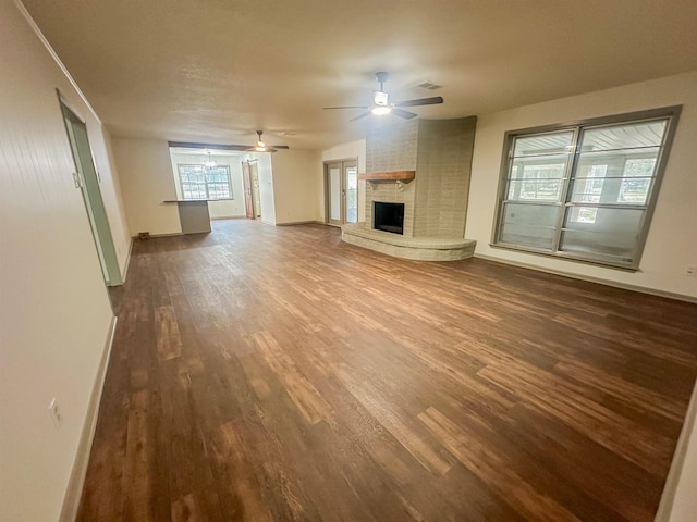 unfurnished living room featuring ceiling fan, a fireplace, baseboards, and dark wood finished floors