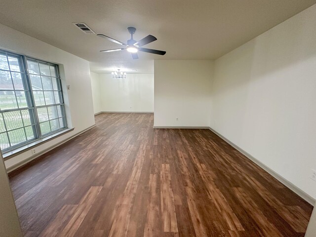 unfurnished room with visible vents, dark wood finished floors, baseboards, and ceiling fan with notable chandelier