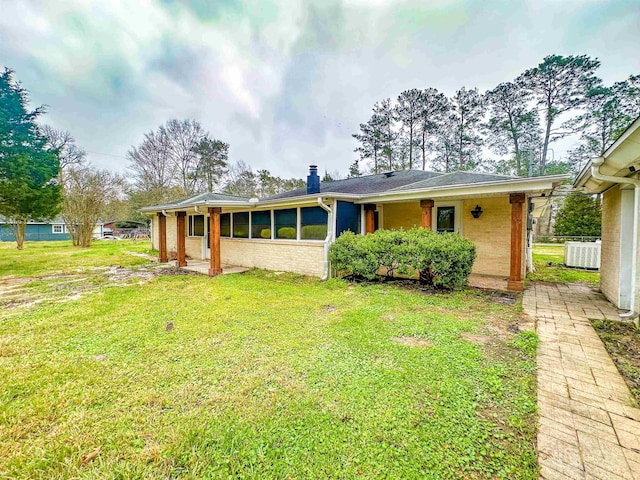 view of front of house featuring brick siding, a chimney, a front yard, and cooling unit