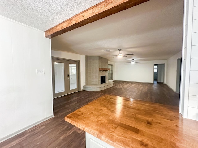 unfurnished living room featuring a brick fireplace, dark wood finished floors, a textured ceiling, and beam ceiling