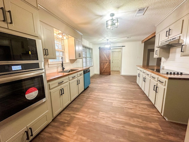 kitchen with butcher block counters, a barn door, a sink, under cabinet range hood, and black appliances