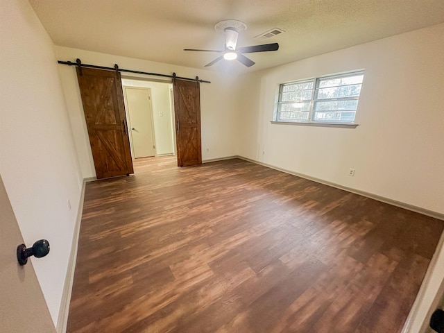 unfurnished bedroom with a barn door, wood finished floors, a ceiling fan, visible vents, and baseboards