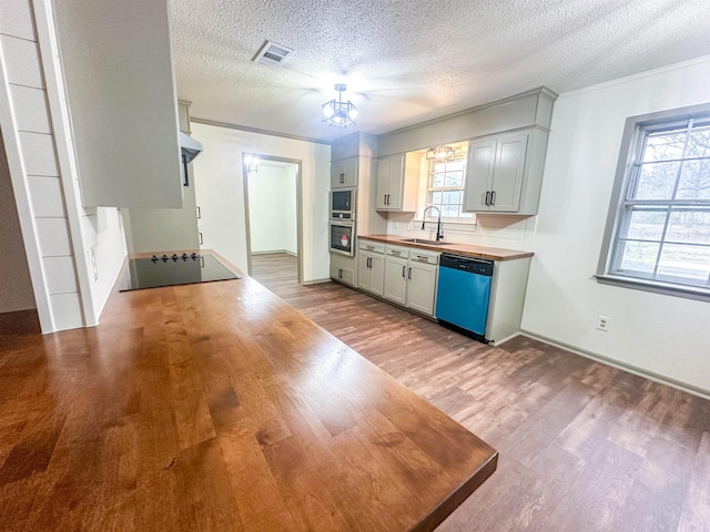 kitchen with dishwashing machine, black electric cooktop, a sink, visible vents, and wood counters