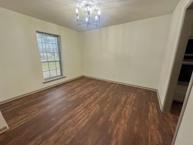 empty room featuring dark wood-style floors, a textured ceiling, a chandelier, and baseboards