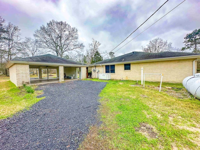 back of house with gravel driveway, brick siding, and a yard