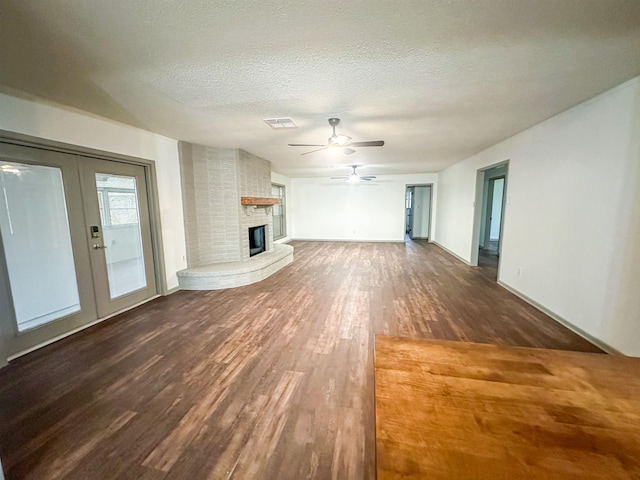 unfurnished living room with a large fireplace, visible vents, a textured ceiling, and wood finished floors