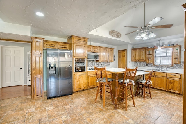 kitchen with a kitchen bar, decorative backsplash, stainless steel appliances, ceiling fan, and sink