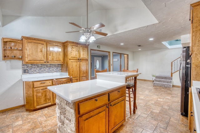 kitchen featuring ceiling fan, lofted ceiling, a kitchen bar, decorative backsplash, and a kitchen island