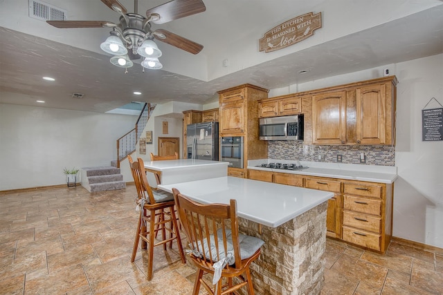 kitchen featuring ceiling fan, a center island, a kitchen bar, decorative backsplash, and appliances with stainless steel finishes