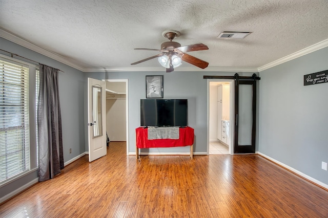 unfurnished living room featuring french doors, light wood-type flooring, ceiling fan, crown molding, and a barn door