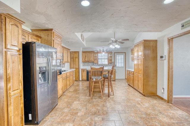 kitchen featuring stainless steel fridge, backsplash, a breakfast bar, ceiling fan, and a center island