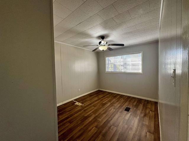 empty room featuring dark hardwood / wood-style flooring, wooden walls, and ceiling fan