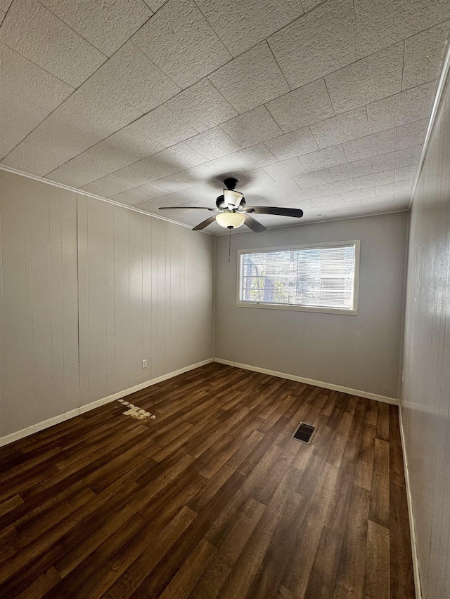 unfurnished room featuring dark wood-type flooring, ceiling fan, and wooden walls