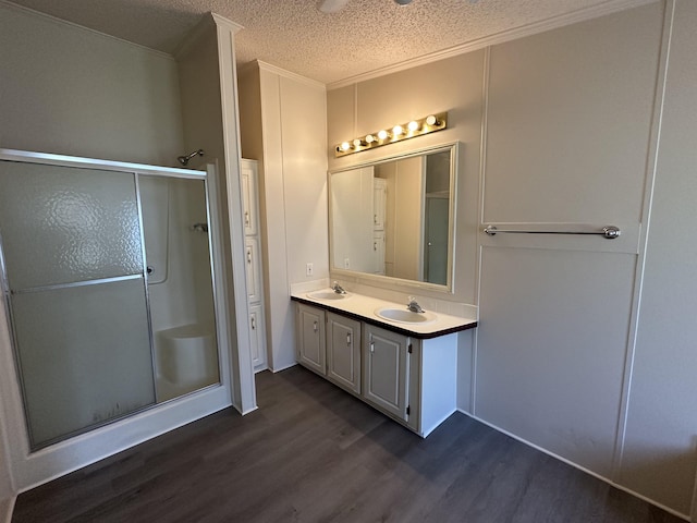 bathroom featuring walk in shower, hardwood / wood-style floors, a textured ceiling, vanity, and ornamental molding