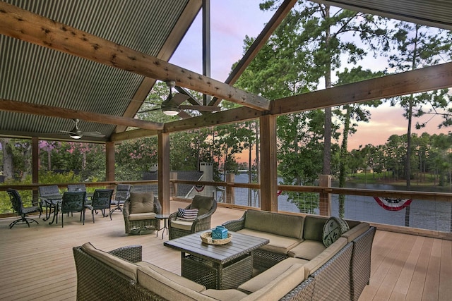 deck at dusk with outdoor lounge area, ceiling fan, and a water view