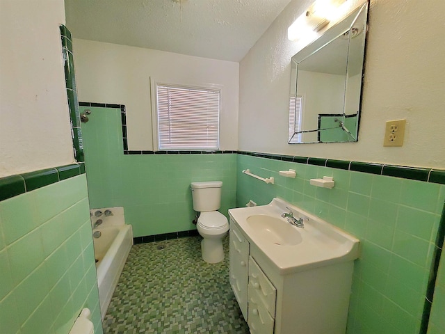 bathroom with vanity, toilet, tile walls, a textured ceiling, and a tub