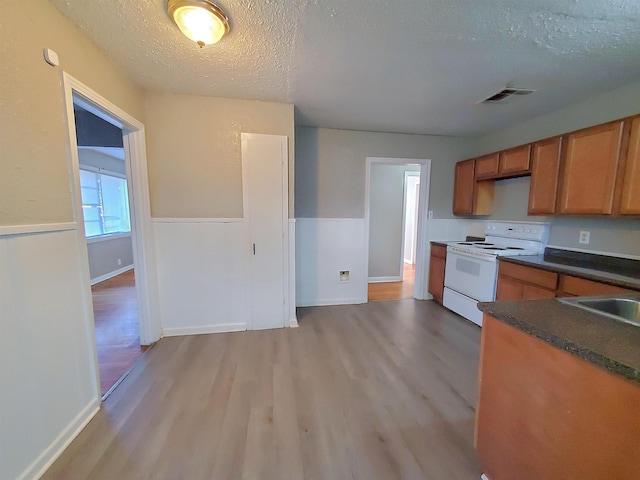 kitchen with white electric range oven, light wood-type flooring, a textured ceiling, and sink