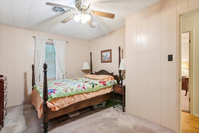 bedroom featuring ceiling fan, wood walls, and light carpet