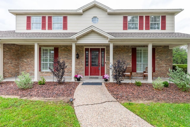 traditional home with a shingled roof, a porch, and brick siding