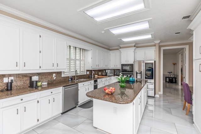 kitchen with white cabinets, a sink, stainless steel appliances, backsplash, and a kitchen island
