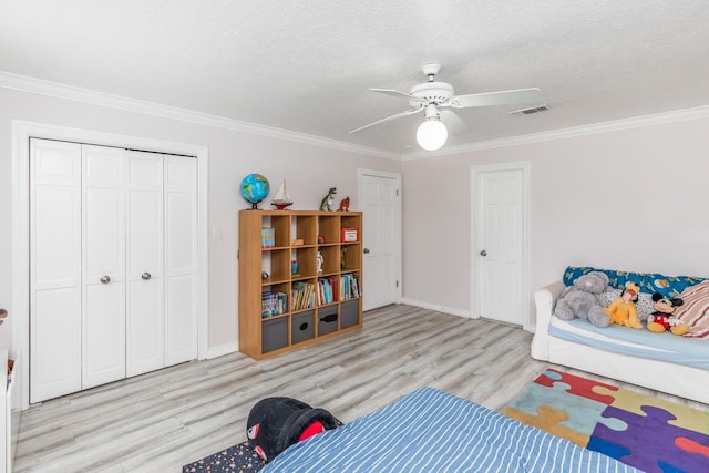 bedroom featuring baseboards, wood finished floors, visible vents, ornamental molding, and a closet