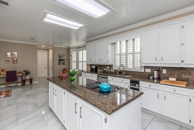 kitchen with white cabinets, a sink, tasteful backsplash, a kitchen island, and visible vents