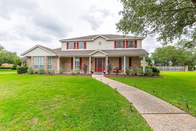 traditional home featuring brick siding, a front yard, and a porch