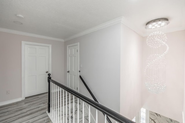 hallway featuring a textured ceiling, baseboards, an upstairs landing, light wood-style floors, and ornamental molding