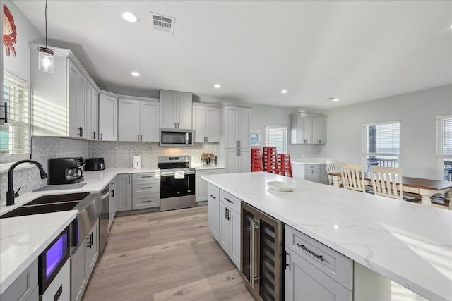 1326 Emerald Dr, Port Bolivar, TX 77650 - kitchen with appliances with stainless steel finishes, beverage cooler, gray cabinetry, light stone countertops, and decorative backsplash