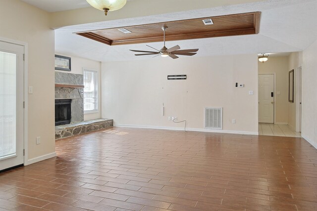 unfurnished living room with a tray ceiling, a stone fireplace, ceiling fan, and wooden ceiling