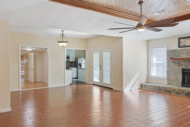 unfurnished living room with a stone fireplace, ceiling fan, and french doors