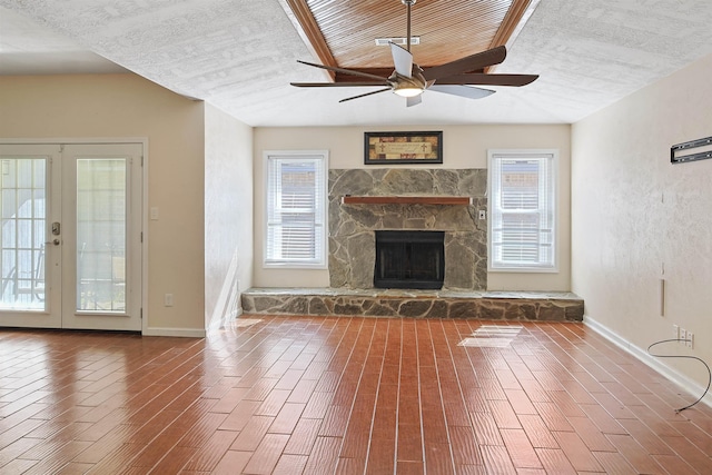 unfurnished living room with a stone fireplace, ceiling fan, french doors, and plenty of natural light