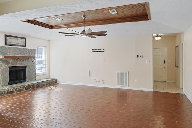 unfurnished living room with a tray ceiling, a stone fireplace, ceiling fan, and wood ceiling