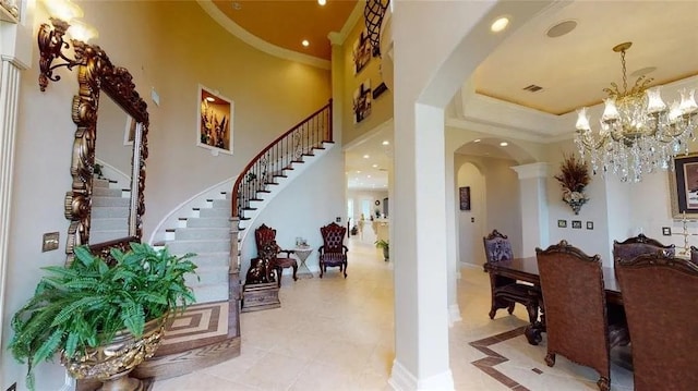 entryway with light tile patterned floors, a high ceiling, a tray ceiling, and an inviting chandelier