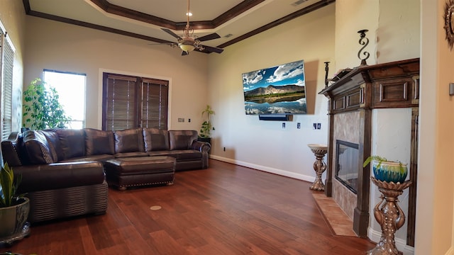 living room with crown molding, baseboards, a fireplace, wood finished floors, and a raised ceiling