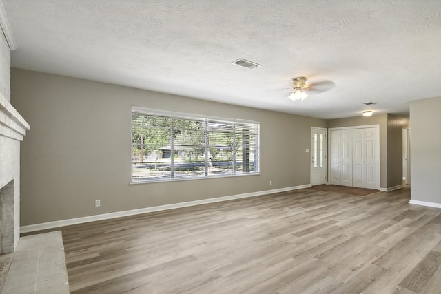 unfurnished living room with a textured ceiling, light wood-type flooring, a brick fireplace, and ceiling fan