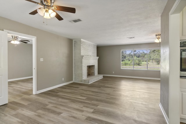 unfurnished living room with ceiling fan, a fireplace, a textured ceiling, and light hardwood / wood-style flooring