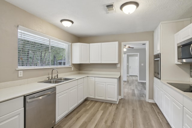 kitchen featuring appliances with stainless steel finishes, light wood-type flooring, a textured ceiling, sink, and white cabinetry