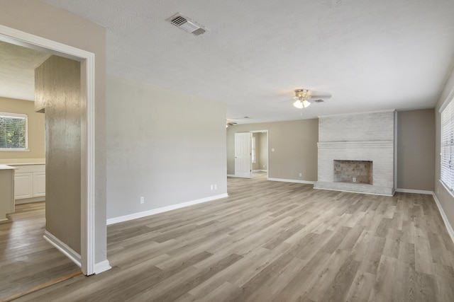 unfurnished living room with ceiling fan, light hardwood / wood-style flooring, a textured ceiling, and a brick fireplace