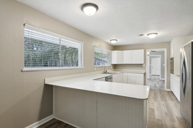 kitchen with white cabinetry, sink, stainless steel appliances, kitchen peninsula, and light wood-type flooring