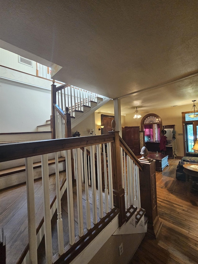 stairway featuring ceiling fan with notable chandelier, wood-type flooring, and a textured ceiling