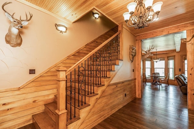 staircase featuring wood walls, crown molding, a notable chandelier, wood-type flooring, and wood ceiling