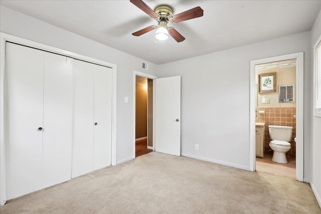 unfurnished bedroom featuring ceiling fan, tile walls, connected bathroom, light carpet, and a closet