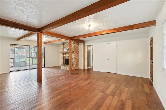 unfurnished living room with a brick fireplace, beam ceiling, hardwood / wood-style floors, and a textured ceiling