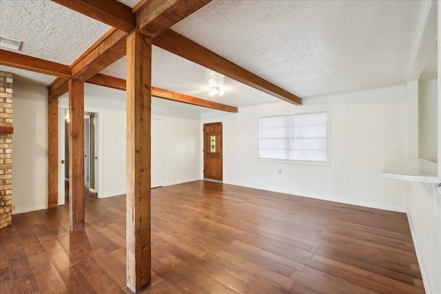 unfurnished living room with dark wood-type flooring, a textured ceiling, and beam ceiling