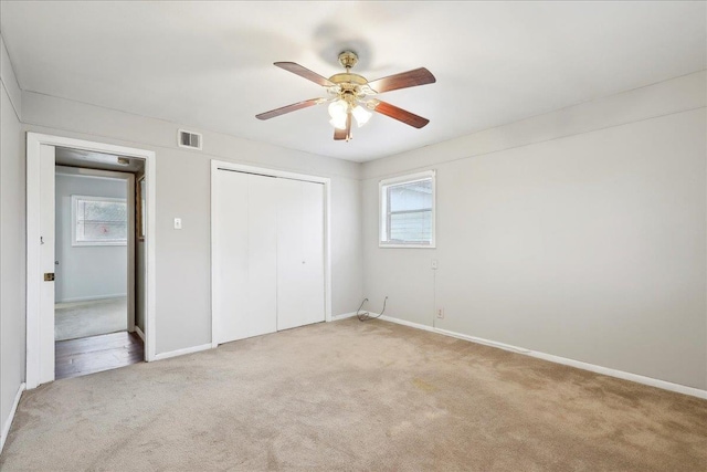 unfurnished bedroom with multiple windows, light carpet, ceiling fan, and a closet