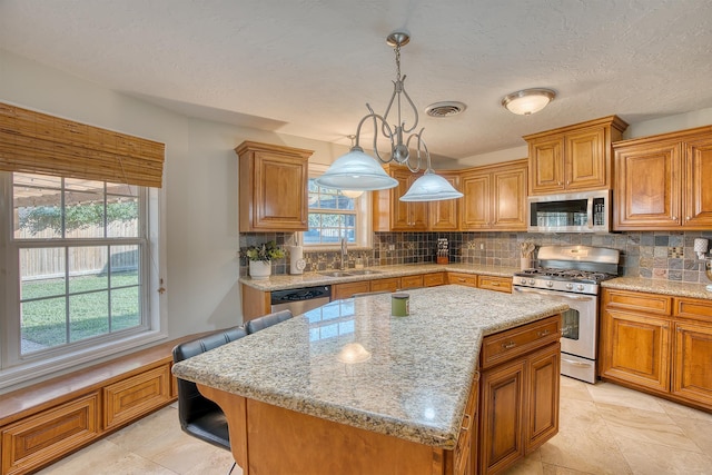 kitchen with light stone counters, stainless steel appliances, sink, a kitchen island, and hanging light fixtures