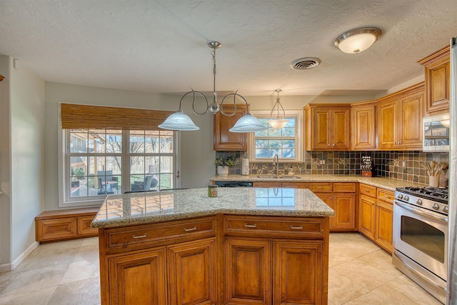 kitchen featuring tasteful backsplash, sink, pendant lighting, stainless steel gas stove, and a kitchen island