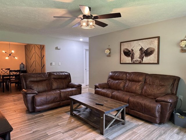 living room featuring a textured ceiling, light wood-style flooring, and ceiling fan with notable chandelier