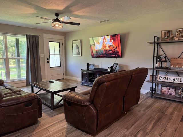 living room featuring ceiling fan, visible vents, baseboards, a textured ceiling, and wood finished floors